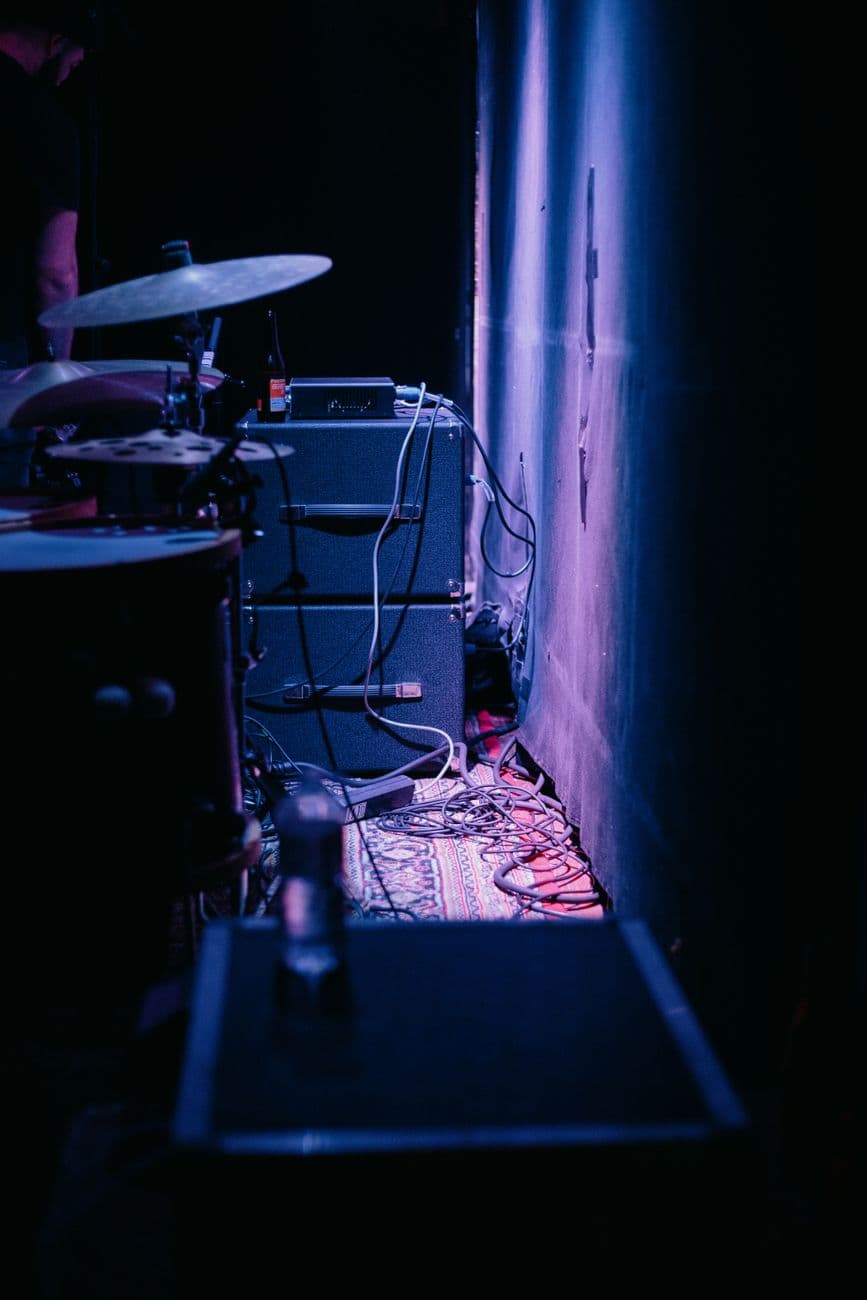 A dark backstage setup with drums and amplifiers in dim lighting, creating a dramatic atmosphere.
