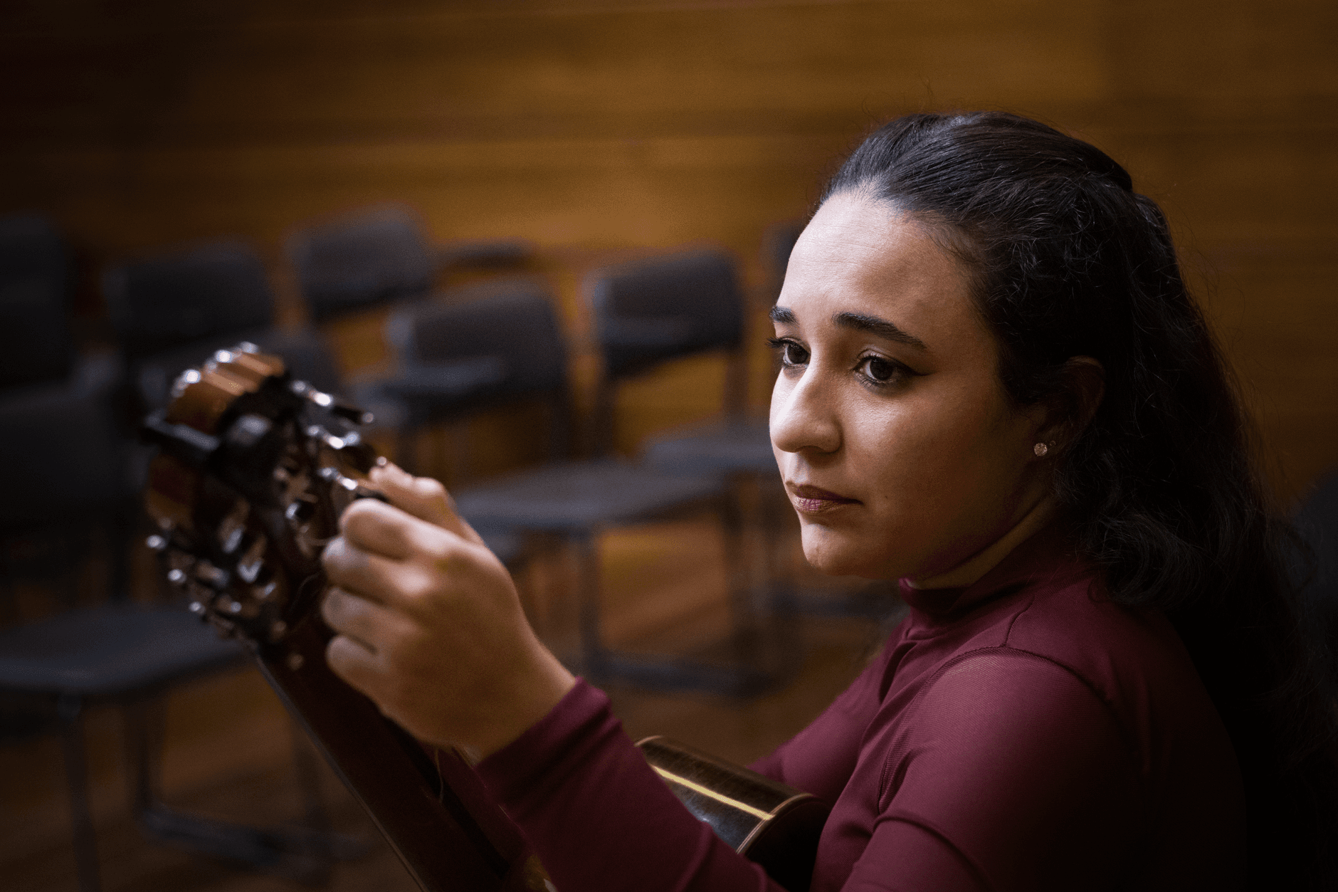 Portrait of a female guitarist in a concert hall, showcasing thoughtful expression with a classical guitar.