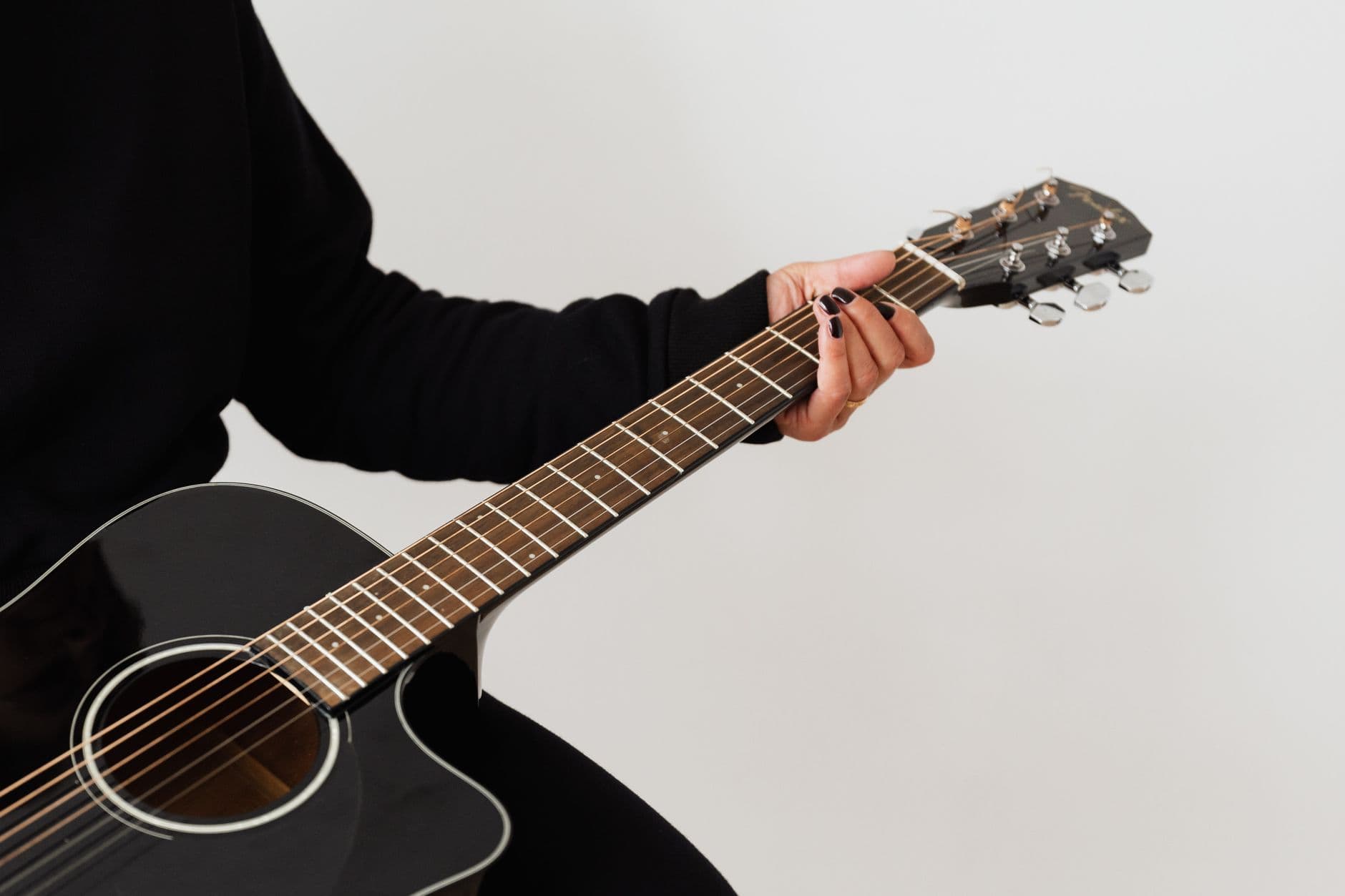 Focused shot of a person holding a black acoustic guitar, showcasing details of the strings and tuning pegs.