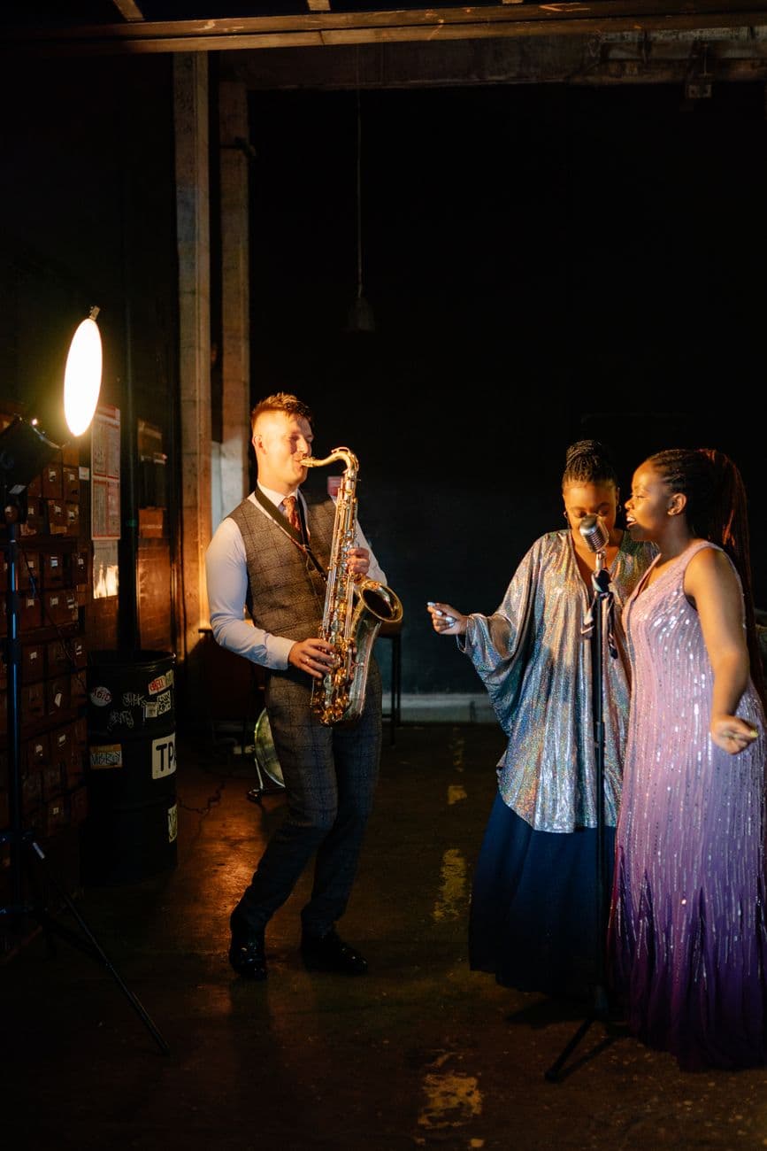 A captivating performance by a saxophonist and two singers on stage, enveloped in elegant lighting.