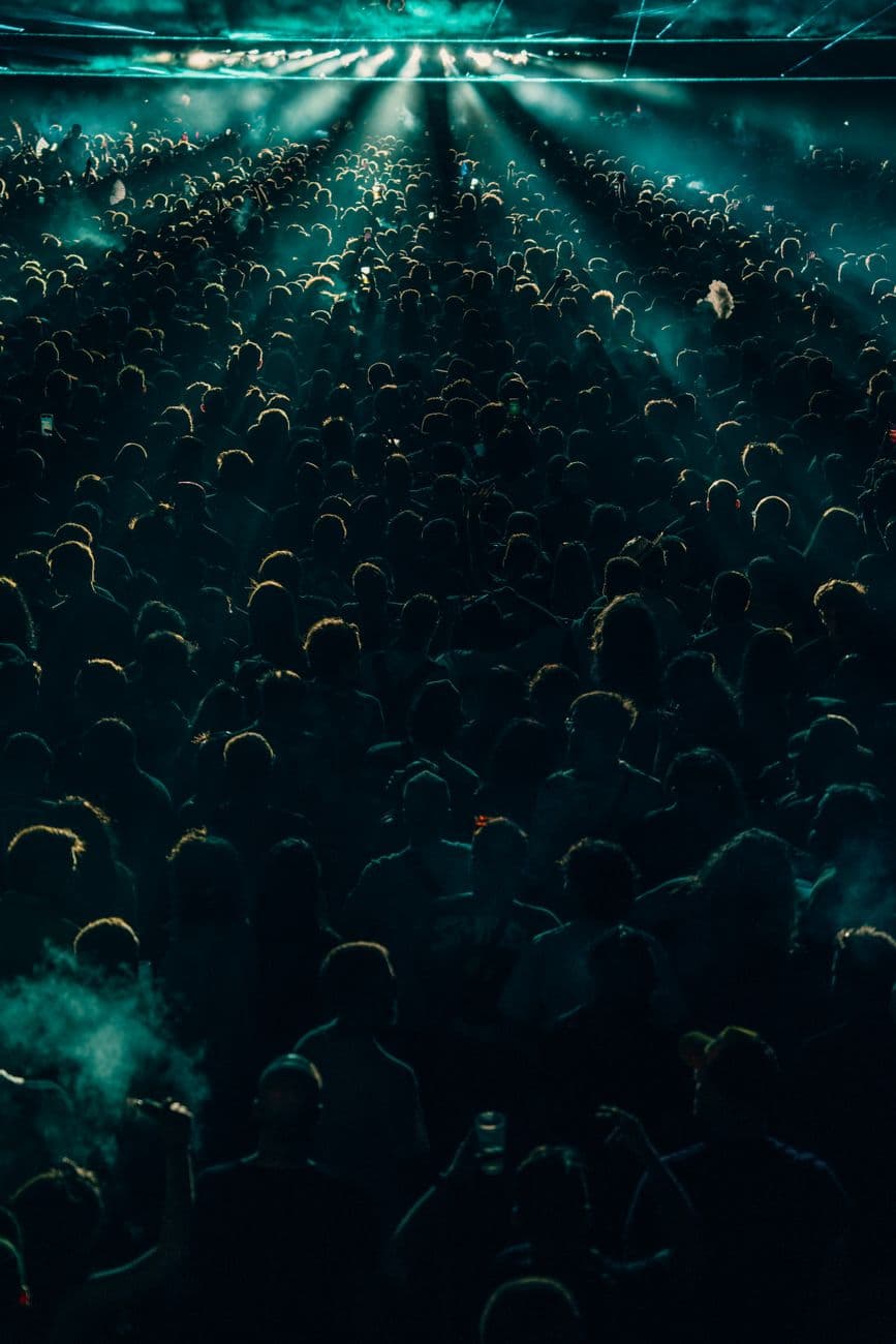 Energetic crowd enjoying a night concert with dramatic lighting effects, creating a lively atmosphere.