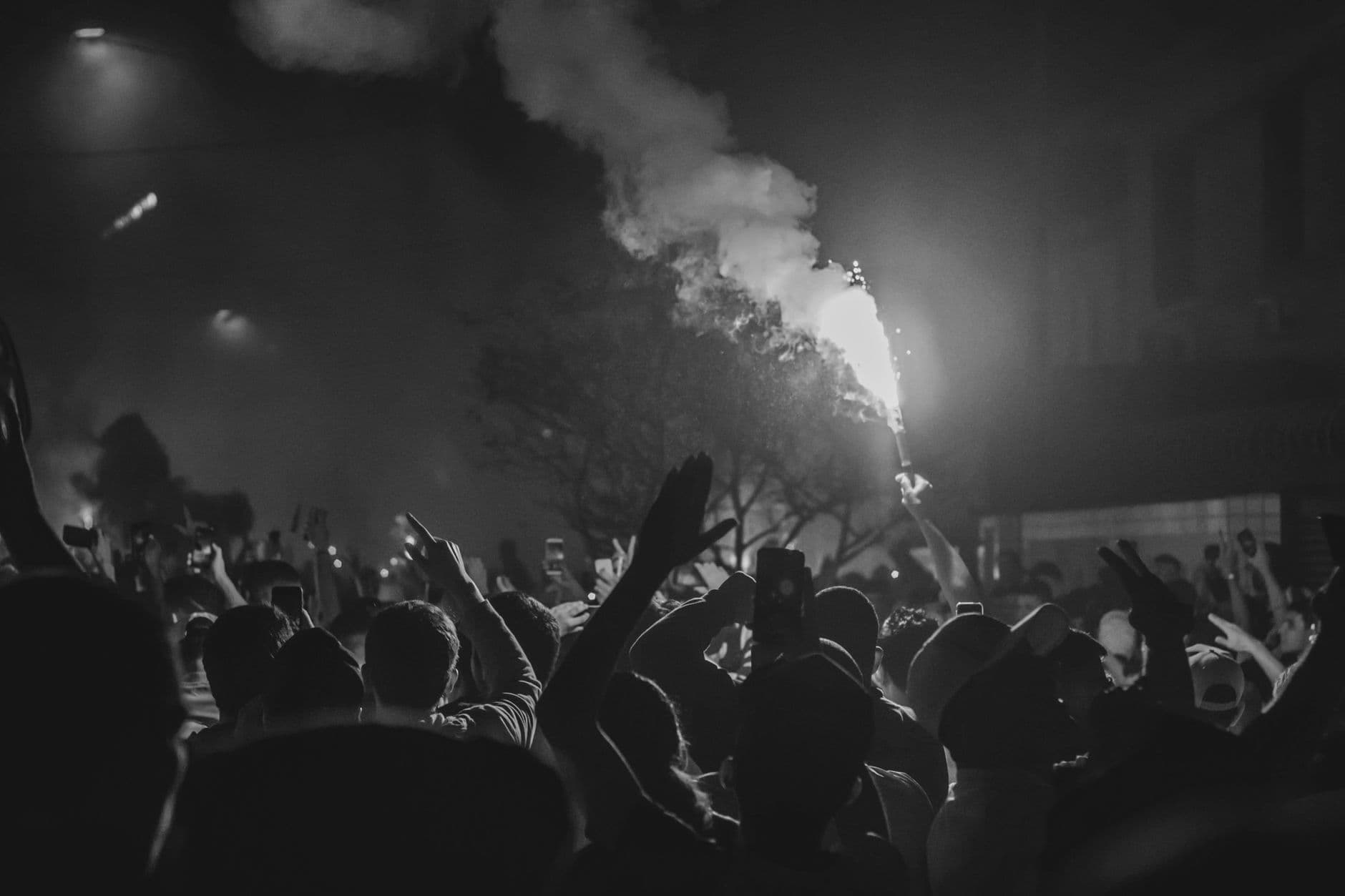 Black and white photo capturing a vibrant crowd at night with smoke and flares, showcasing energy and solidarity.