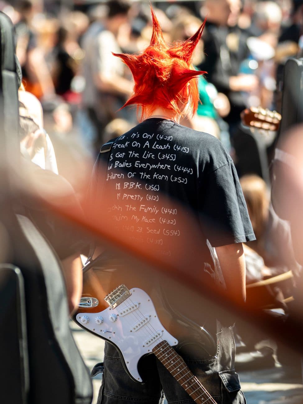 A street performer with a unique hairstyle holding an electric guitar at an outdoor concert in Wrocław.