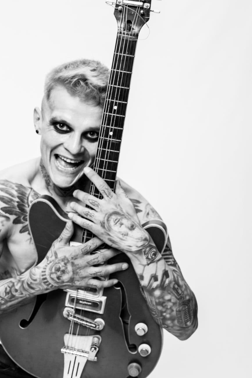 Expressive black & white portrait of a tattooed guitarist with an electric guitar, showcasing rock spirit.