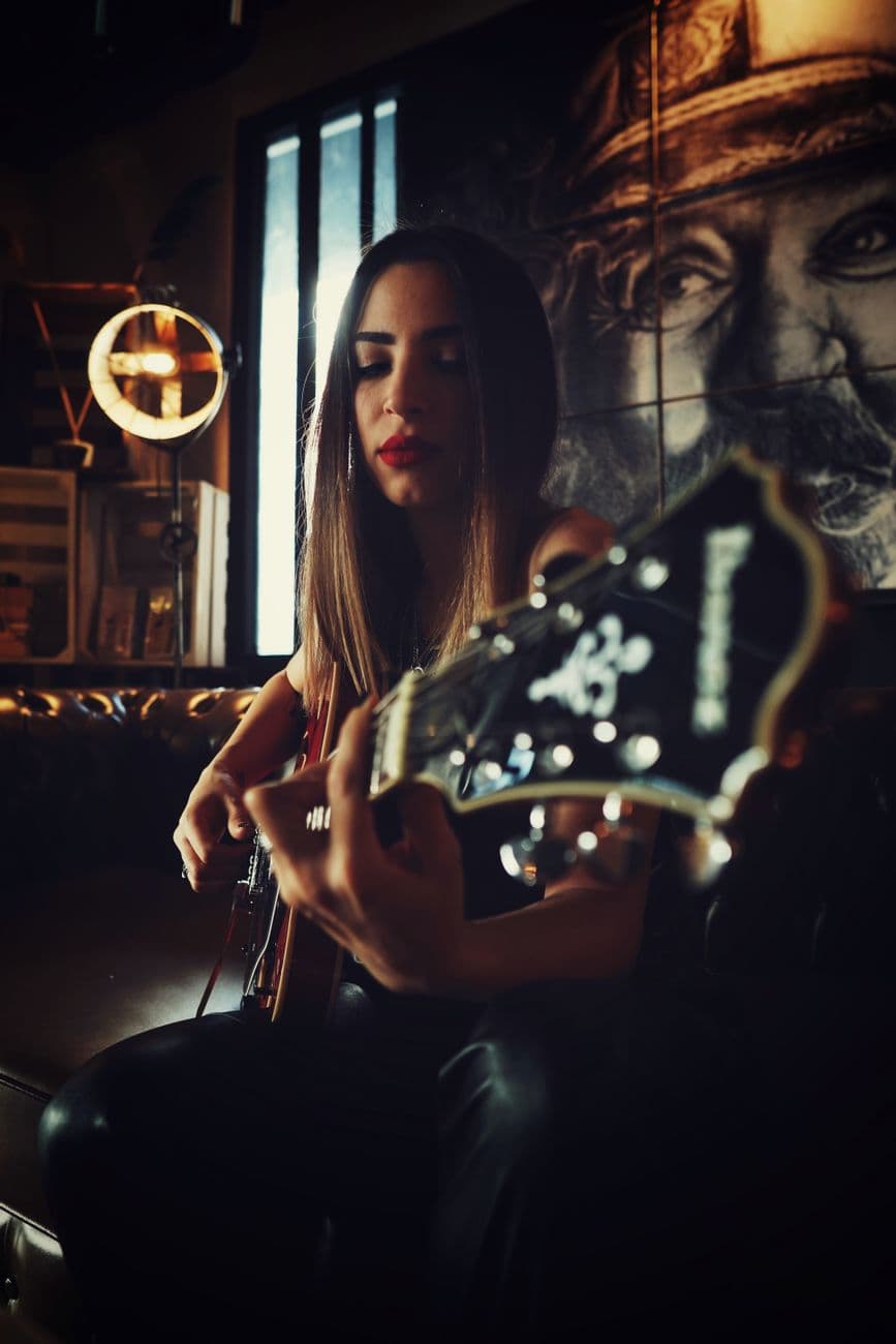 A woman skillfully plays an electric guitar in a dimly lit, artistic indoor setting, capturing a moody musical moment.