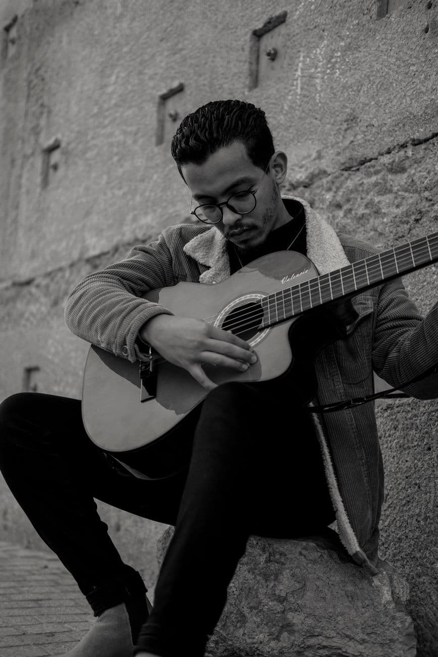 A young man plays acoustic guitar against a stone wall in Rabat, offering a serene street performance.